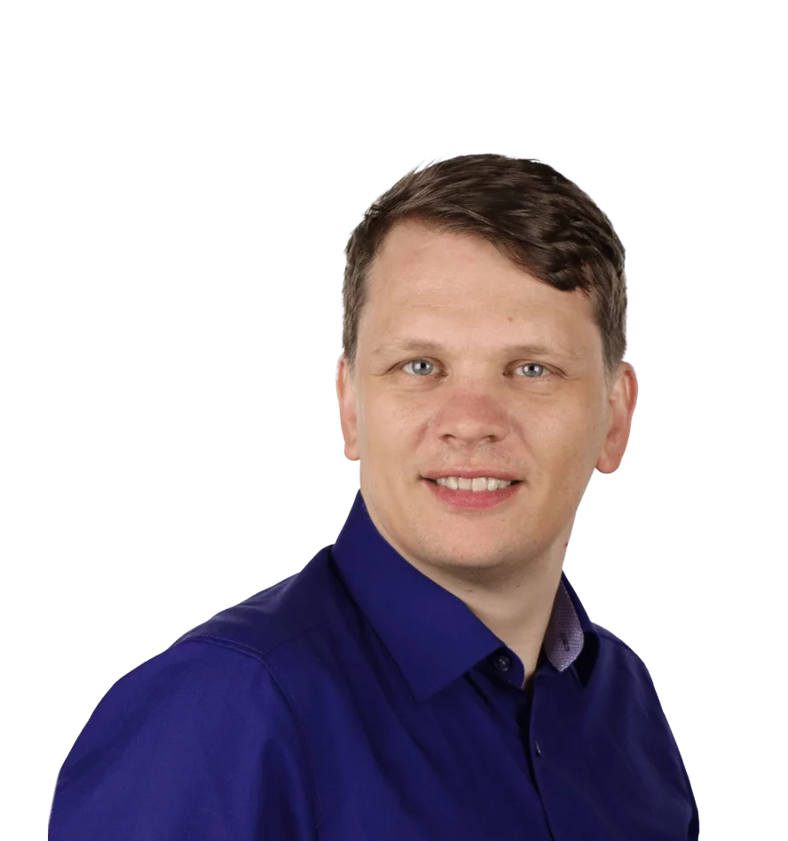Das Bild zeigt einen Mann mittleren Alters, der direkt in die Kamera lächelt. Er hat kurzes, braunes Haar und trägt ein dunkelblaues Hemd. Seine Augen sind blau, und sein Gesichtsausdruck ist freundlich und offen. Der Hintergrund ist weiß, wodurch der Fokus vollständig auf dem Mann liegt.