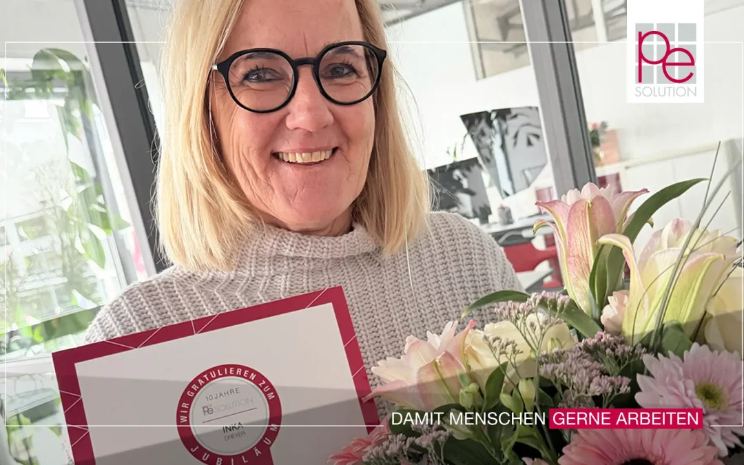 Inka Dreyer von PE Solution mit Blumenstrauß und Jubiläumsurkunde zum 10-jährigen Firmenjubiläum.